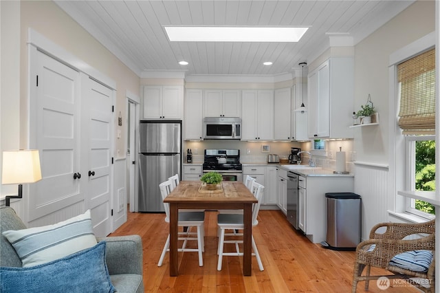 17 Beach Cabin Ln, Pacific Beach, WA 98571 - kitchen with stainless steel appliances, a skylight, white cabinets, light wood-type flooring, and ornamental molding