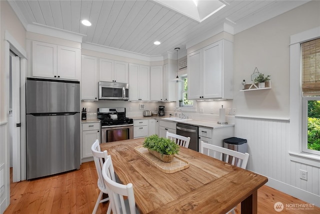 17 Beach Cabin Ln, Pacific Beach, WA 98571 - kitchen with stainless steel appliances, white cabinetry, ornamental molding, light wood finished floors, and a wainscoted wall