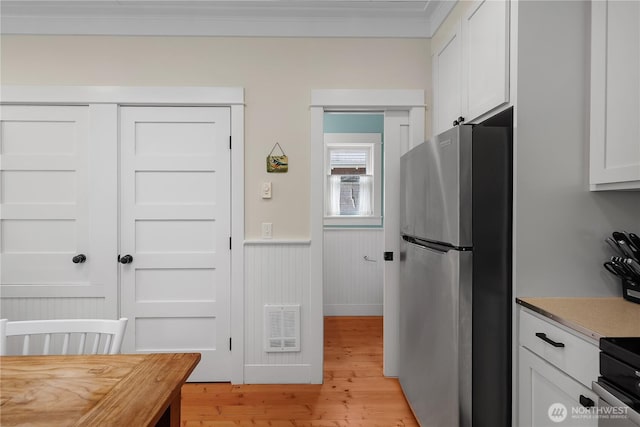 17 Beach Cabin Ln, Pacific Beach, WA 98571 - kitchen featuring stainless steel appliances, a wainscoted wall, crown molding, light wood-style flooring, and white cabinetry