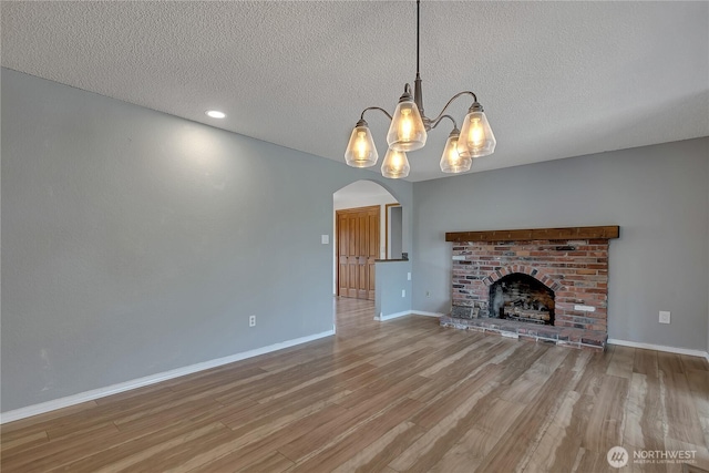 622 119th Ave E, Edgewood, WA 98372 - unfurnished living room with wood finished floors, a chandelier, a textured ceiling, arched walkways, and a brick fireplace