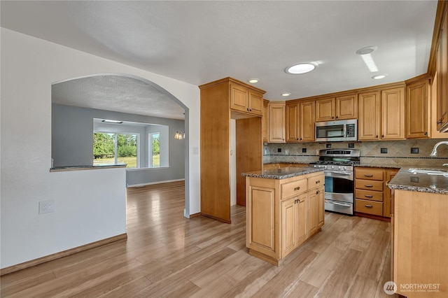 622 119th Ave E, Edgewood, WA 98372 - kitchen featuring stainless steel appliances, arched walkways, dark stone counters, tasteful backsplash, and light wood finished floors