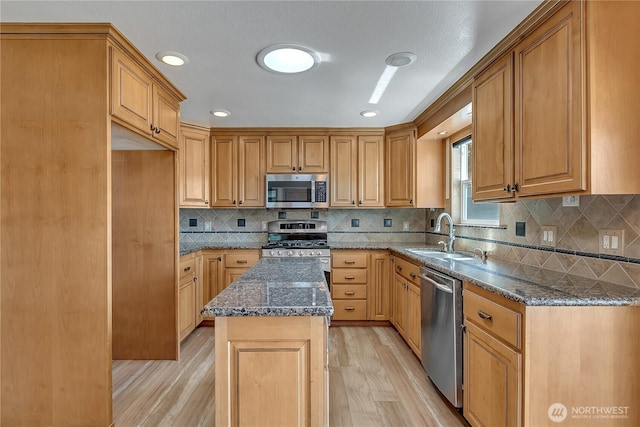 622 119th Ave E, Edgewood, WA 98372 - kitchen featuring appliances with stainless steel finishes, light wood-style floors, dark stone countertops, decorative backsplash, and a center island