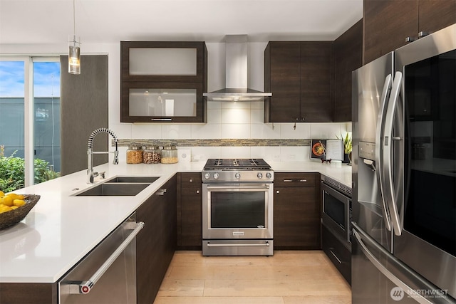 909 29th Ave S, Seattle, WA 98144 - kitchen featuring appliances with stainless steel finishes, wall chimney range hood, dark brown cabinets, a peninsula, and light wood-style flooring