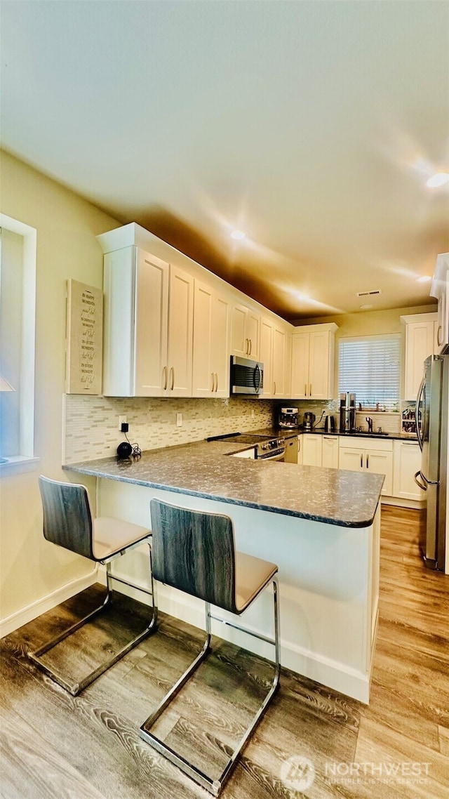 23884 NE 112th Cir Unit 2, Redmond, WA 98053 - kitchen with stainless steel appliances, a peninsula, light wood-type flooring, white cabinets, and a breakfast bar