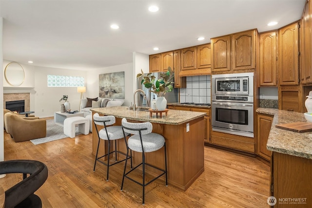 1417 232nd Pl SW, Bothell, WA 98021 - kitchen with appliances with stainless steel finishes, a kitchen bar, brown cabinets, open floor plan, and light stone counters