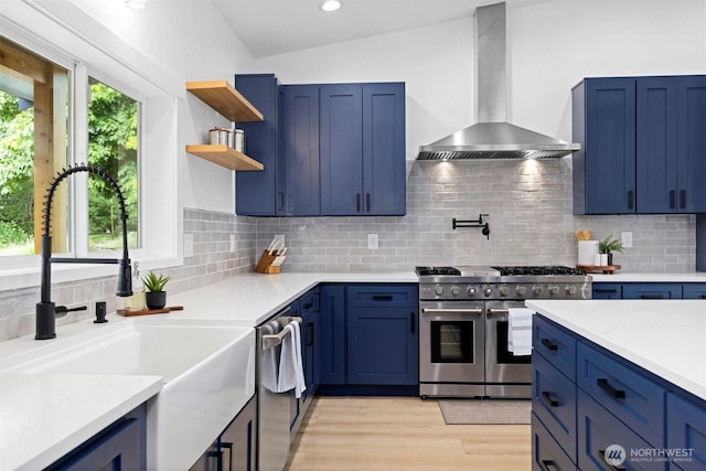 2403 E Hemmi Rd, Bellingham, WA 98226 - kitchen featuring wall chimney exhaust hood, stainless steel appliances, blue cabinets, light wood-style flooring, and backsplash