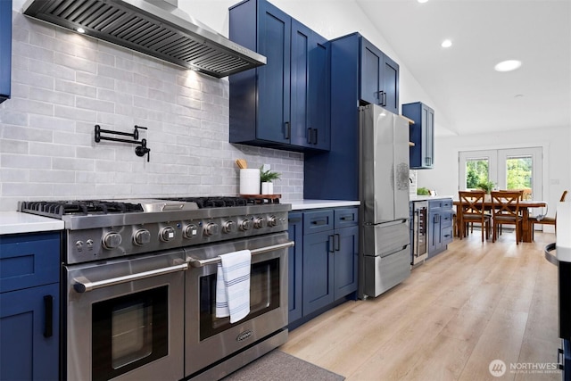 2403 E Hemmi Rd, Bellingham, WA 98226 - kitchen with appliances with stainless steel finishes, wall chimney exhaust hood, blue cabinets, light countertops, and light wood finished floors