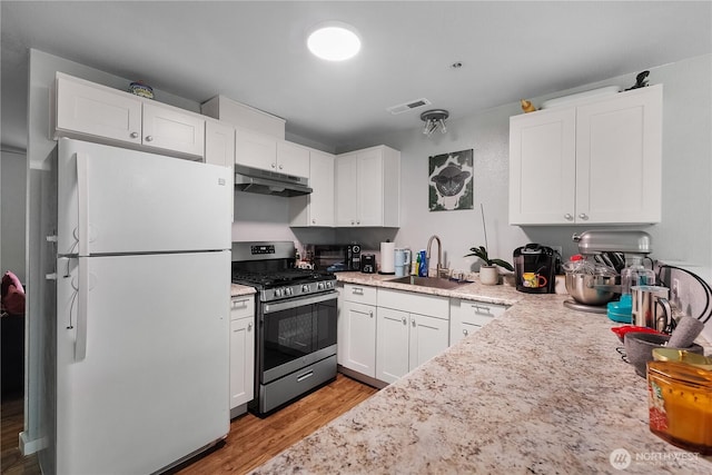 1222 Cora St SE, Lacey, WA 98503 - kitchen with freestanding refrigerator, stainless steel gas range oven, under cabinet range hood, light wood-style floors, and white cabinetry