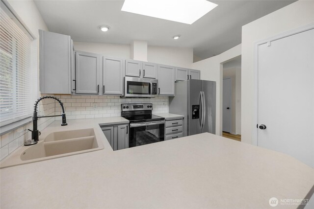 8618 217th Pl NE, Arlington, WA 98223 - kitchen with stainless steel appliances, a skylight, tasteful backsplash, light countertops, and gray cabinets
