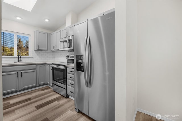 8618 217th Pl NE, Arlington, WA 98223 - kitchen with appliances with stainless steel finishes, a skylight, gray cabinets, tasteful backsplash, and light wood-style floors