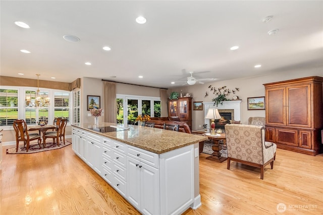 3912 Prestwick Ln SE, Olympia, WA 98501 - kitchen with light wood finished floors, a kitchen island, a warm lit fireplace, a chandelier, and white cabinetry