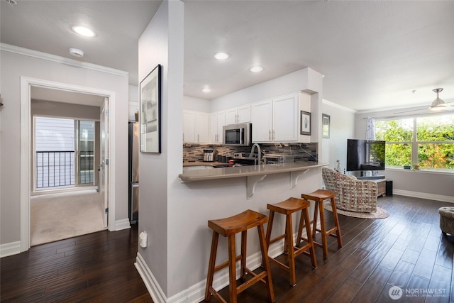 960 Harris Ave Unit 305, Bellingham, WA 98225 - kitchen with stainless steel appliances, dark wood-style flooring, white cabinetry, a kitchen breakfast bar, and decorative backsplash