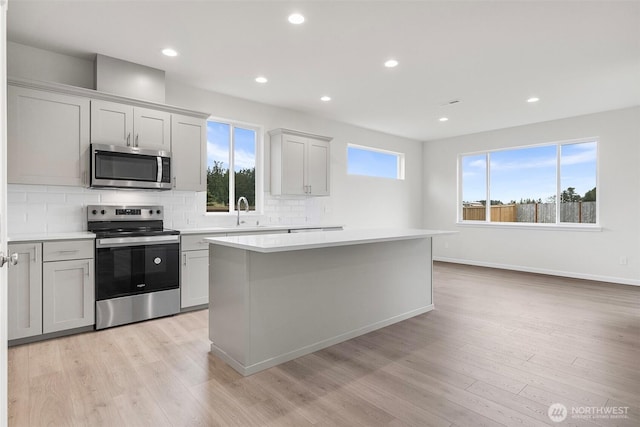 14756 88th Way SE Unit 10, Yelm, WA 98597 - kitchen with appliances with stainless steel finishes, a center island, tasteful backsplash, light countertops, and light wood finished floors
