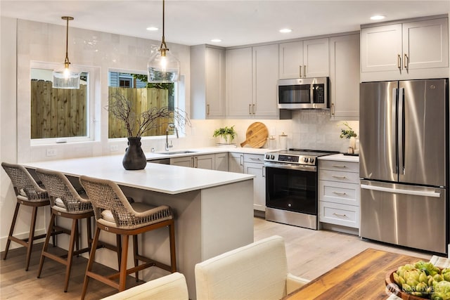 2616 E Roy St, Seattle, WA 98112 - kitchen featuring appliances with stainless steel finishes, light wood-type flooring, a peninsula, light countertops, and a kitchen bar