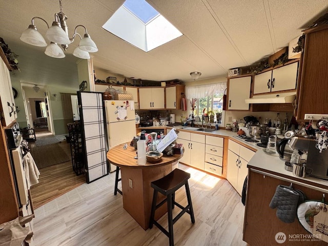 8839 Daffodil Ln SE, Olympia, WA 98513 - kitchen featuring under cabinet range hood, light wood finished floors, a skylight, a chandelier, and pendant lighting