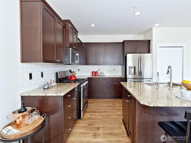 16271 SE 181st St, Renton, WA 98058 - kitchen featuring appliances with stainless steel finishes, light wood-style flooring, a kitchen breakfast bar, light stone counters, and backsplash