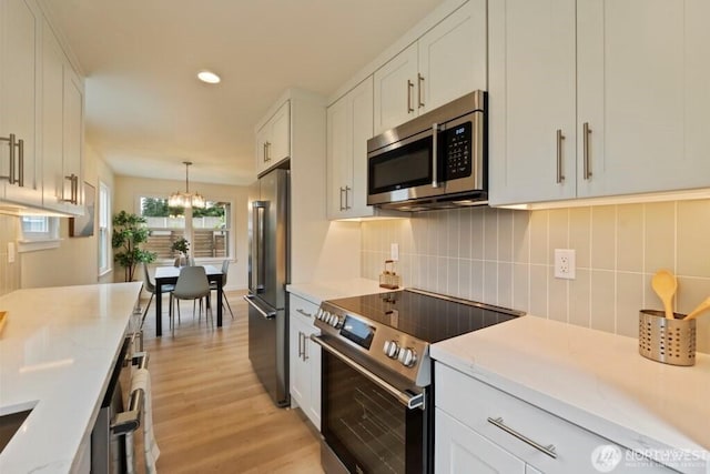 12302 5th Ave NE, Seattle, WA 98125 - kitchen featuring stainless steel appliances, a chandelier, white cabinets, light wood finished floors, and tasteful backsplash