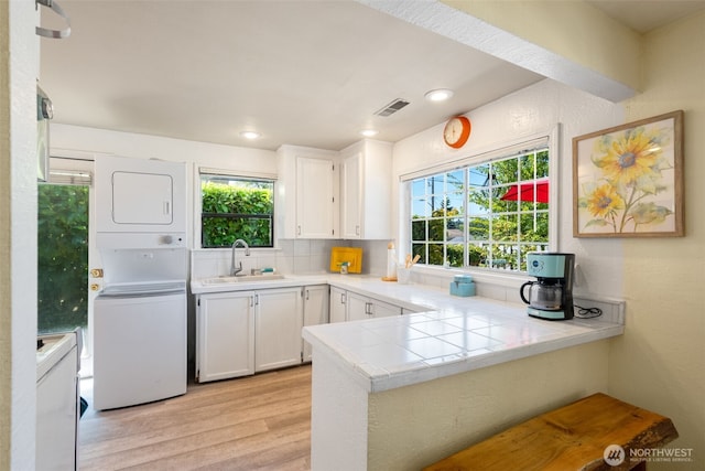 1524 30th Ave, Seattle, WA 98122 - kitchen with stacked washing machine and dryer, light wood-style floors, white cabinets, healthy amount of natural light, and recessed lighting