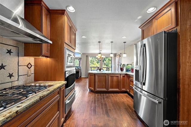 21410 SE 265th Pl, Maple Valley, WA 98038 - kitchen with stainless steel appliances, wall chimney range hood, a peninsula, brown cabinetry, and light stone countertops