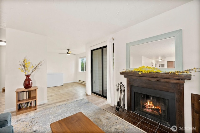 303 Kenyon St NW Unit 2D, Olympia, WA 98502 - living room featuring wood finished floors, a warm lit fireplace, ceiling fan, and a baseboard radiator