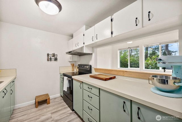 303 Kenyon St NW Unit 2D, Olympia, WA 98502 - kitchen with black range with electric stovetop, under cabinet range hood, light countertops, light wood finished floors, and white cabinetry