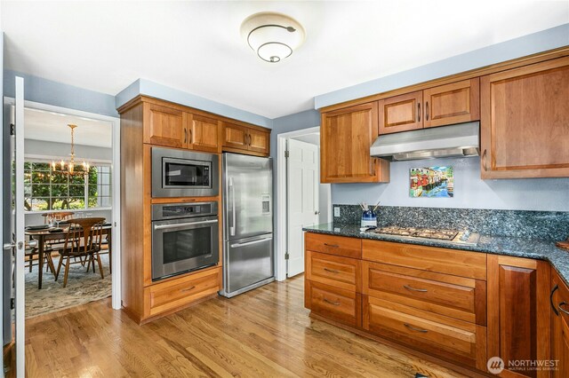 1023 144th Pl SE, Bellevue, WA 98007 - kitchen featuring stainless steel appliances, under cabinet range hood, light wood finished floors, brown cabinetry, and a chandelier