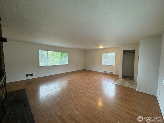 16425 Broadway Ave, Snohomish, WA 98296 - unfurnished living room with a baseboard heating unit, healthy amount of natural light, wood finished floors, and a textured ceiling