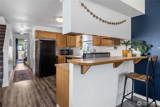 1949 S Sheridan Ave, Tacoma, WA 98405 - kitchen with black appliances, a peninsula, a kitchen bar, dark wood finished floors, and brown cabinetry