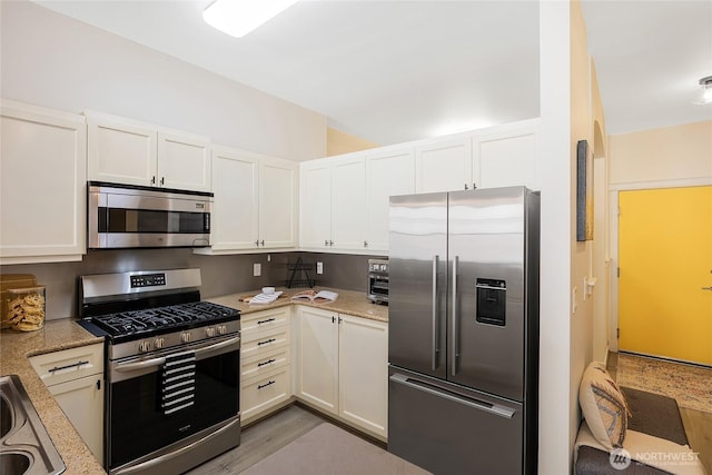 530 4th Ave W Unit 405, Seattle, WA 98119 - kitchen featuring appliances with stainless steel finishes, white cabinetry, light wood-style floors, and light stone counters