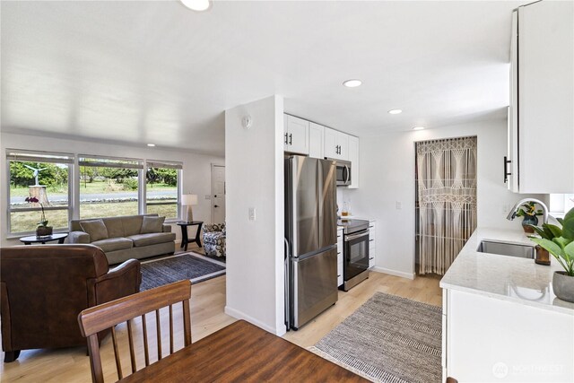2426 Haines St, Port Townsend, WA 98368 - kitchen with stainless steel appliances, white cabinets, open floor plan, light wood-style floors, and light stone counters