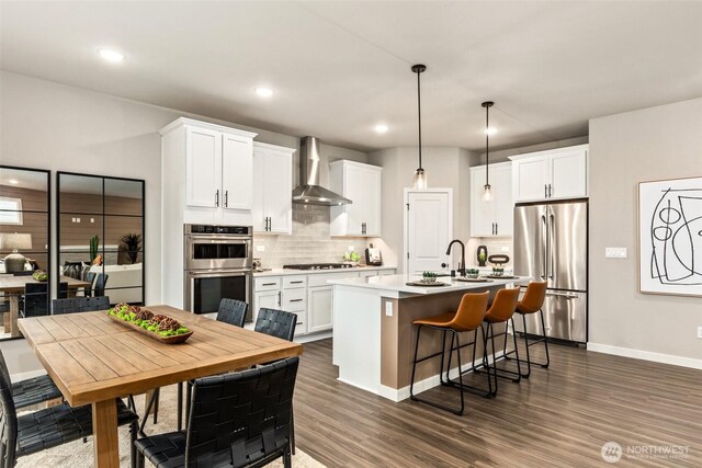 32324 135th Pl SE Unit 211, Sultan, WA 98294 - kitchen with appliances with stainless steel finishes, wall chimney exhaust hood, decorative backsplash, a kitchen island with sink, and white cabinets