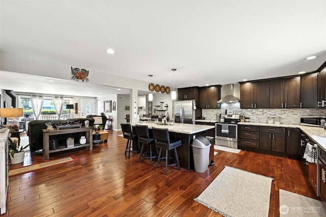 7212 188th Ave E, Bonney Lake, WA 98391 - kitchen featuring appliances with stainless steel finishes, wall chimney range hood, open floor plan, dark brown cabinets, and recessed lighting