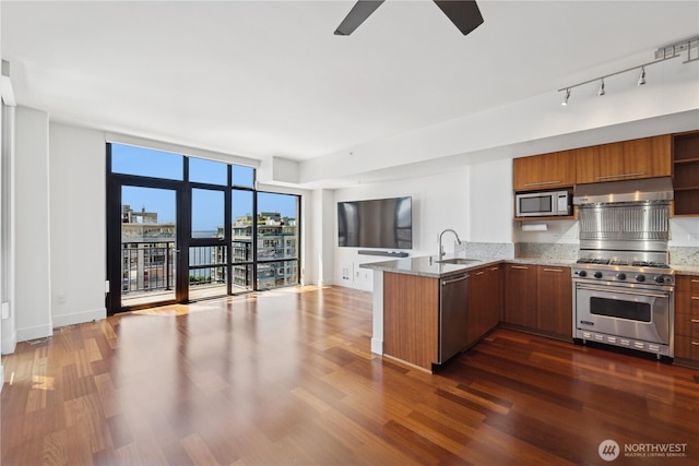 2911 2nd Ave Unit 1117, Seattle, WA 98121 - kitchen with stainless steel appliances, a peninsula, brown cabinetry, a ceiling fan, and dark wood-type flooring