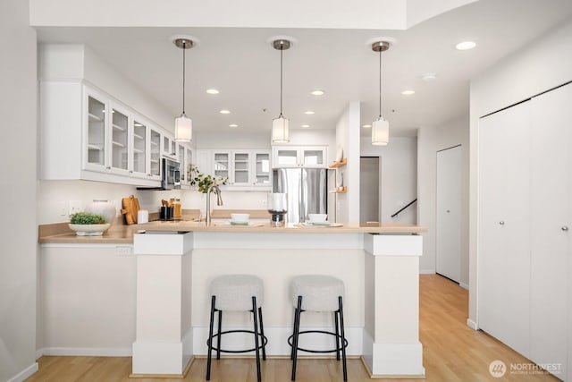 2400 8th Ave N Unit 2, Seattle, WA 98109 - kitchen with appliances with stainless steel finishes, a peninsula, light wood finished floors, a breakfast bar, and white cabinets
