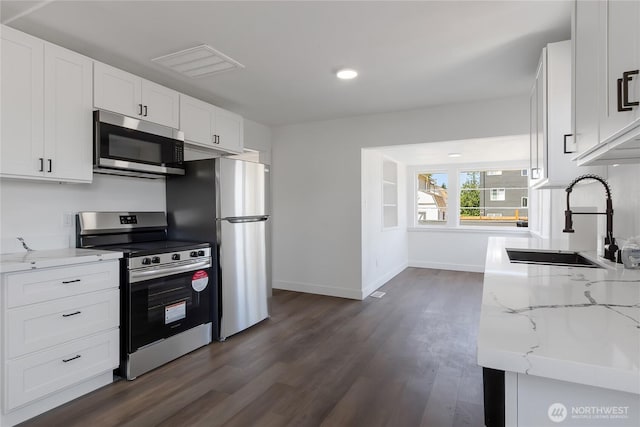 1433 E 32nd St, Tacoma, WA 98404 - kitchen with appliances with stainless steel finishes, dark wood-style flooring, light stone countertops, white cabinetry, and recessed lighting