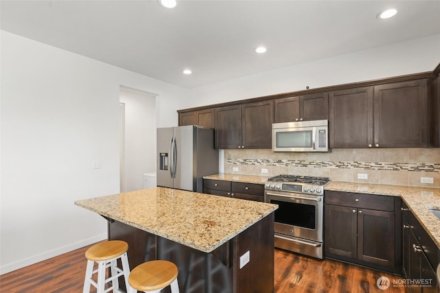 6821 9th St E, Fife, WA 98424 - kitchen with appliances with stainless steel finishes, dark brown cabinetry, dark wood-style floors, decorative backsplash, and a kitchen bar