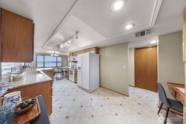 9727 NE Juanita Dr Unit 308, Kirkland, WA 98034 - kitchen with white appliances, brown cabinetry, a tray ceiling, a textured ceiling, and rail lighting