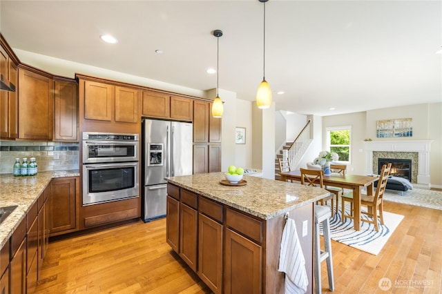 1501 209th Ave NE, Sammamish, WA 98074 - kitchen featuring appliances with stainless steel finishes, light wood-style floors, a glass covered fireplace, light stone counters, and hanging light fixtures