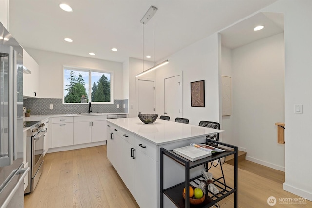 1323 N 185th St Unit A, Shoreline, WA 98133 - kitchen with appliances with stainless steel finishes, light wood-style floors, backsplash, white cabinets, and a center island