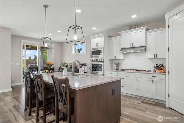 1118 26th St NW, Puyallup, WA 98373 - kitchen with appliances with stainless steel finishes, under cabinet range hood, light wood-style flooring, light countertops, and white cabinetry