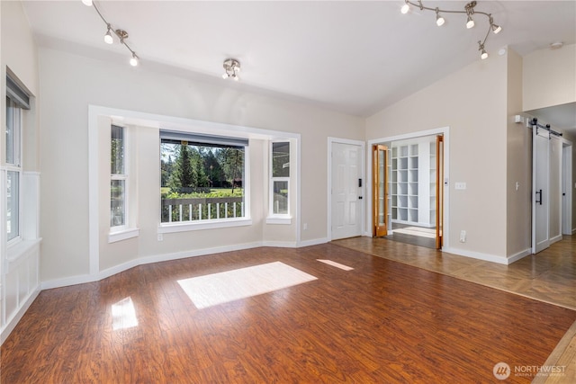120 E Rd Of Tralee, Shelton, WA 98584 - unfurnished living room featuring rail lighting, vaulted ceiling, a barn door, and wood finished floors