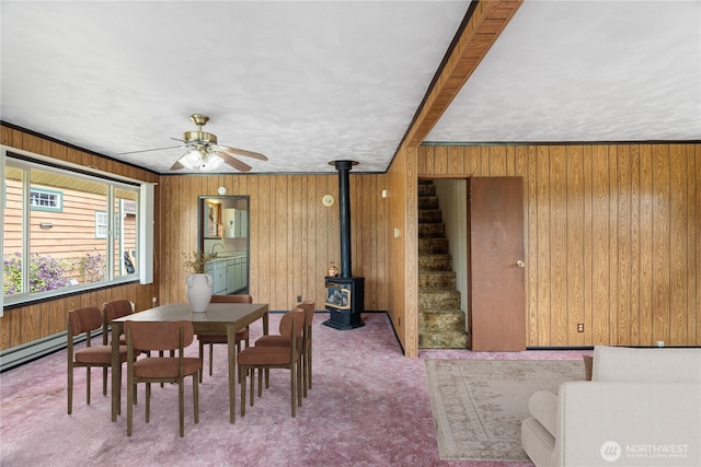 2507 Bay Ave, Hoquiam, WA 98550 - carpeted dining room featuring a wood stove, wood walls, stairs, a ceiling fan, and a baseboard heating unit
