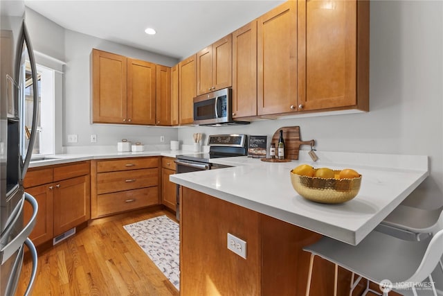 3055 49th Ave SW, Seattle, WA 98116 - kitchen featuring stainless steel appliances, light wood finished floors, a peninsula, a kitchen bar, and light countertops