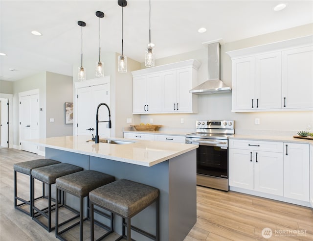 884 NE Tyler Pl E, Wenatchee, WA 98802 - kitchen with stainless steel range with electric stovetop, wall chimney range hood, a kitchen bar, light wood-style flooring, and white cabinetry