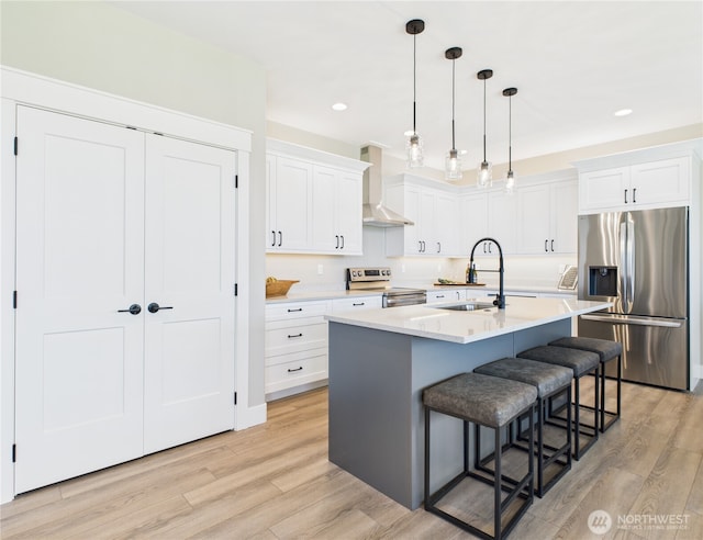 884 NE Tyler Pl E, Wenatchee, WA 98802 - kitchen featuring appliances with stainless steel finishes, wall chimney exhaust hood, light wood-style flooring, a breakfast bar, and white cabinetry