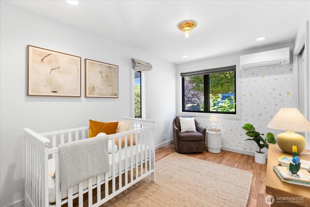 8733 21st Ave NW, Seattle, WA 98117 - bedroom with a wall mounted air conditioner, wood finished floors, a nursery area, recessed lighting, and wallpapered walls
