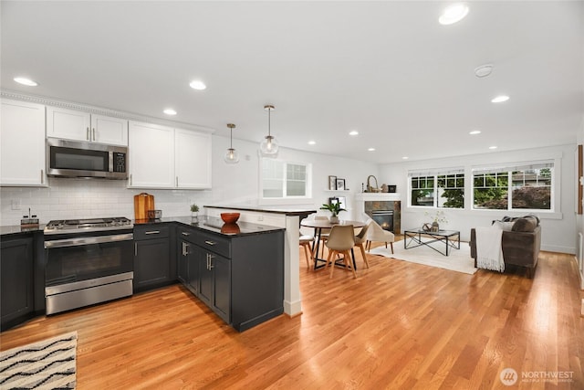 9217 Roosevelt Way NE Unit B, Seattle, WA 98115 - kitchen featuring stainless steel appliances, dark countertops, white cabinets, a peninsula, and light wood-style floors