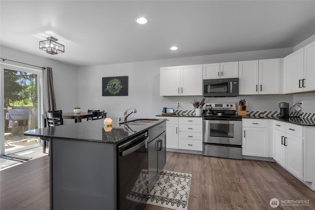 19826 207th Street Ct E, Orting, WA 98360 - kitchen with stainless steel appliances, recessed lighting, wood finished floors, a center island with sink, and dark stone countertops