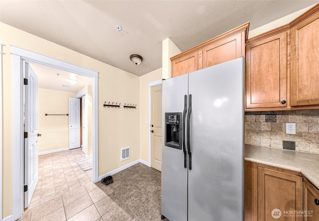 690 32nd St Unit B210, Bellingham, WA 98225 - kitchen featuring stainless steel fridge, backsplash, light countertops, light tile patterned flooring, and brown cabinetry