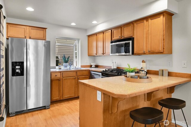 1542 15th Ave S Unit A, Seattle, WA 98144 - kitchen with appliances with stainless steel finishes, a peninsula, brown cabinetry, light wood-style floors, and recessed lighting